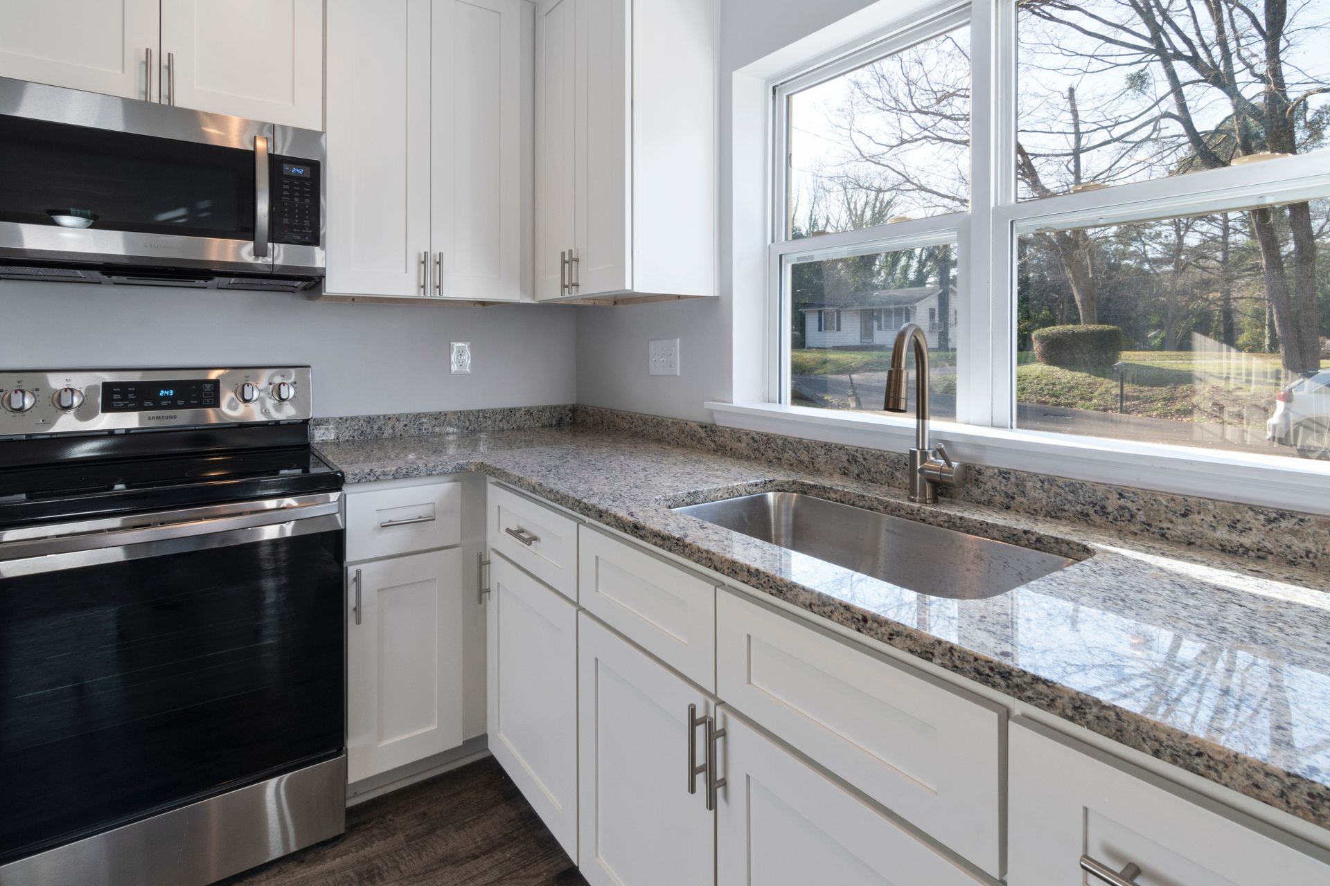 Bright kitchen showcasing granite countertops, stainless steel appliances, and large windows.